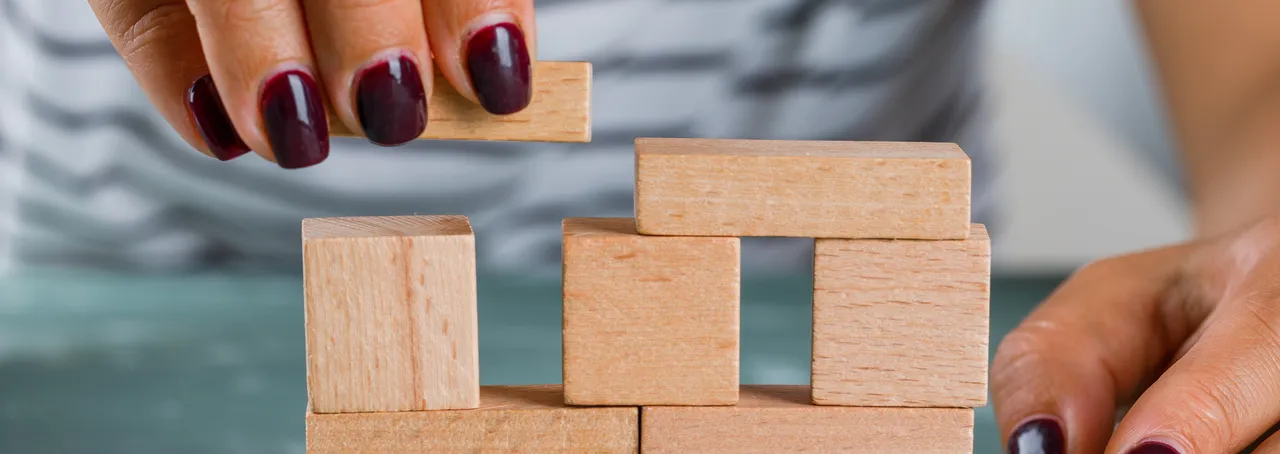 Hands placing wooden blocks to build a small tower on a table.