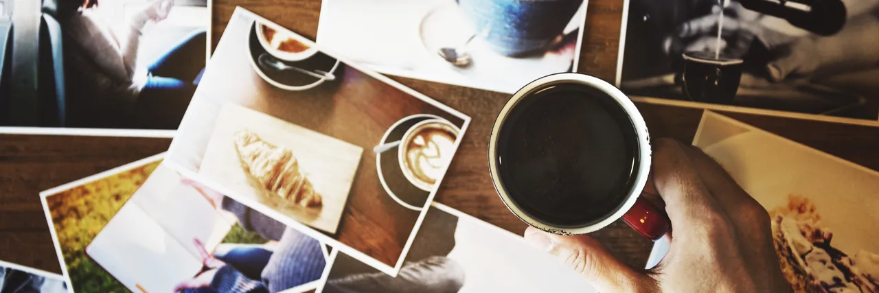 A hand holding a mug of coffee over a table covered in printed photographs.