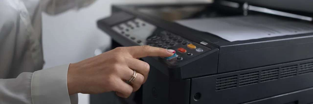 A woman in an office pressing a button on a photocopier with its lid open.